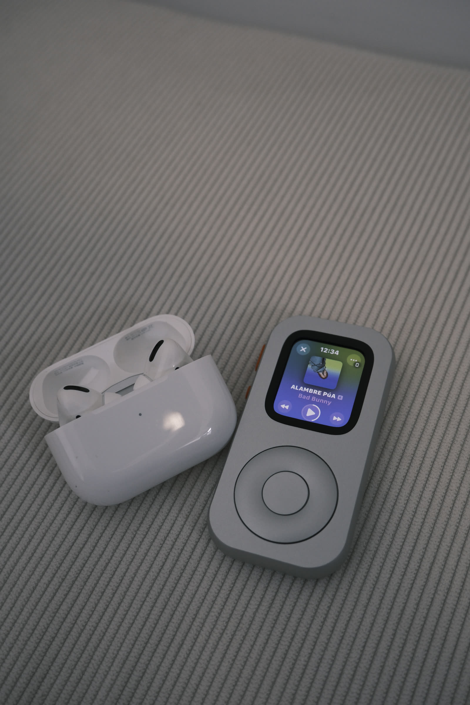 A front-facing RePod beside open AirPods with music playback visible on the Apple Watch screen