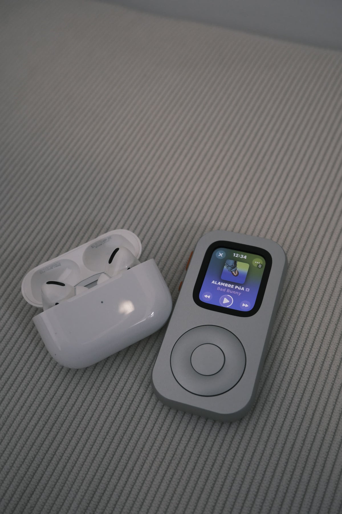 A front-facing RePod beside open AirPods with music playback visible on the Apple Watch screen