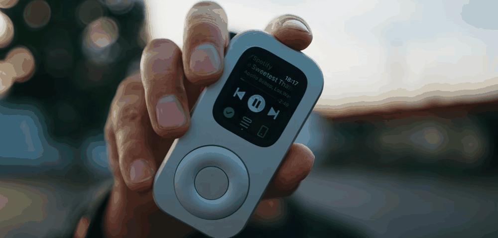 A hand holds a front-facing RePod with music playback visible during a commute.