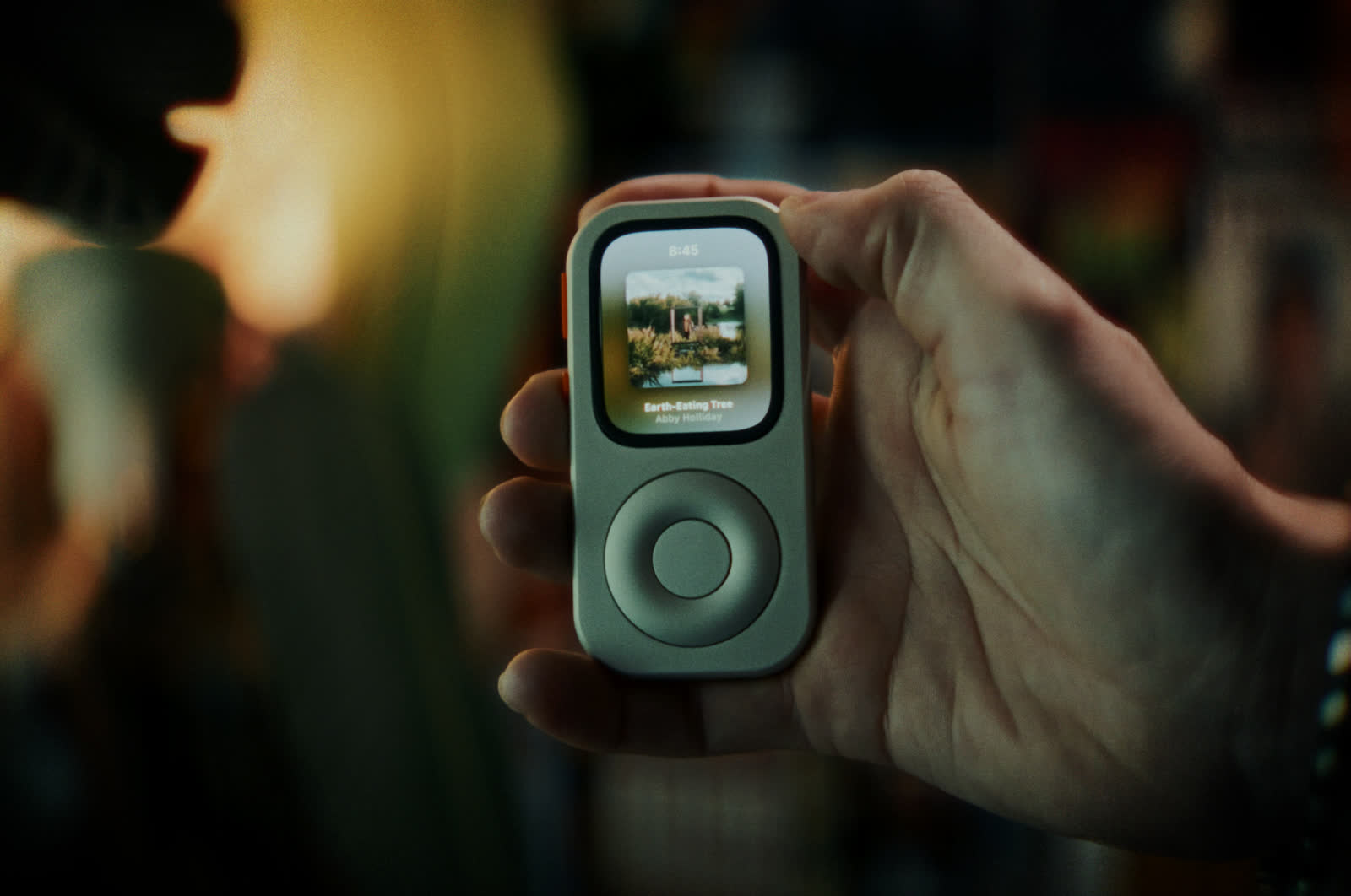 A front-facing RePod held in one hand with music controls visible on the Apple Watch screen