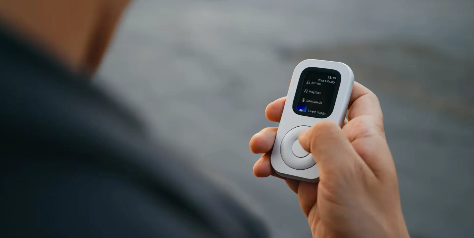 Hand holding RePod outdoors with an Apple Watch music screen visible