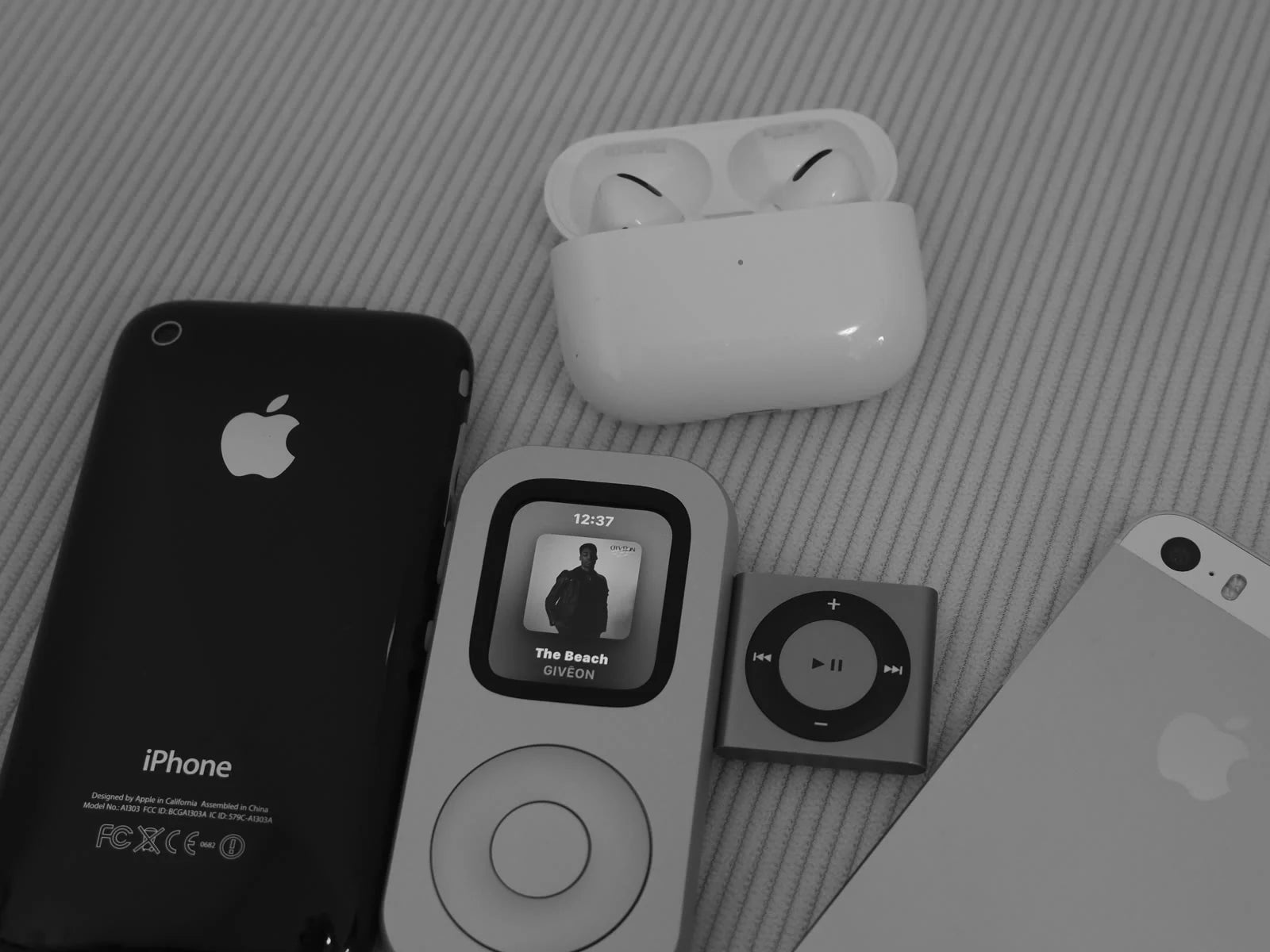 Front view of RePod displaying music beside older Apple devices, an iPod shuffle and AirPods